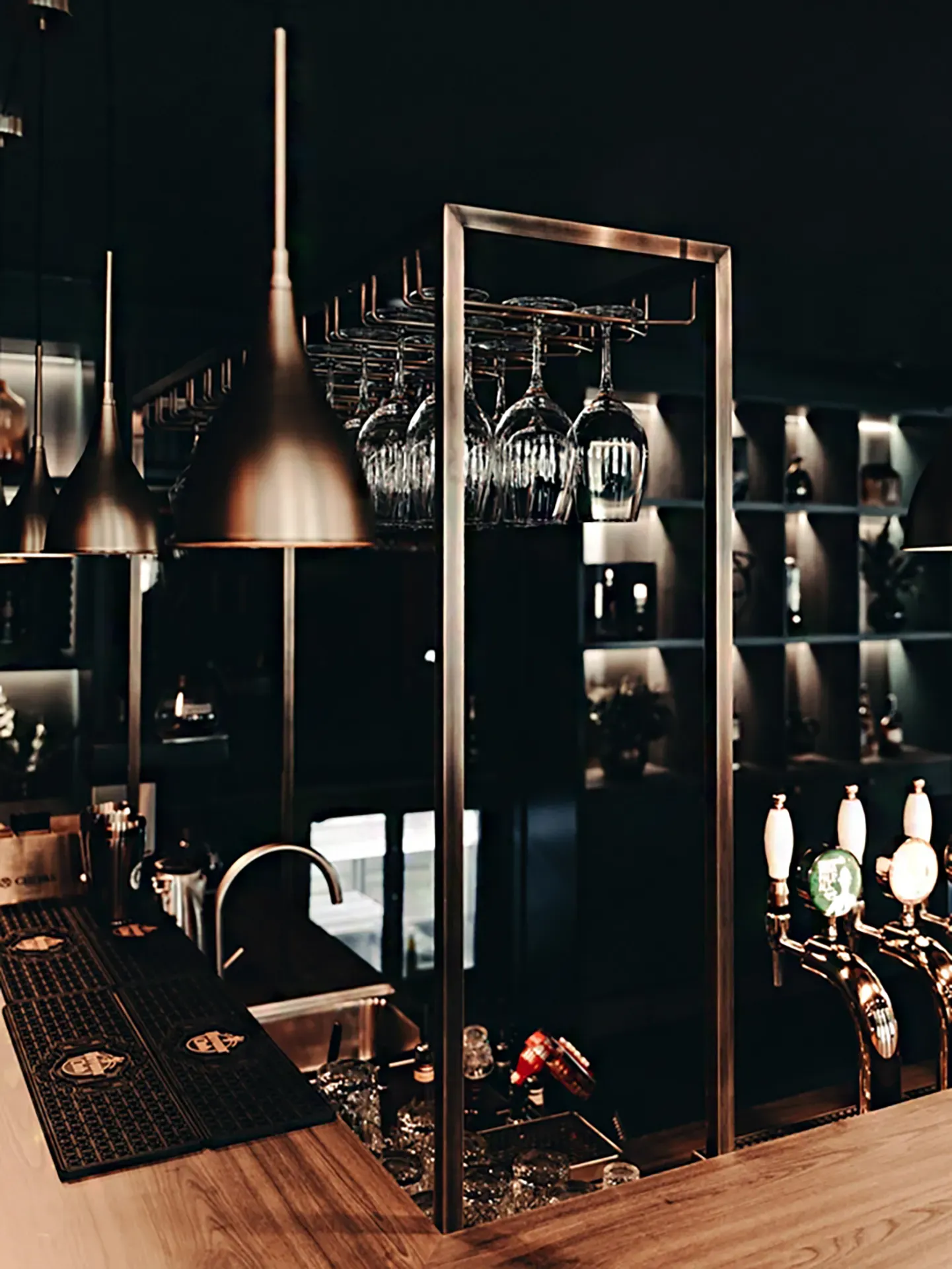 Detail of brass lighting and glassware racks in a custom hospitality bar interior at Hotel Royal.