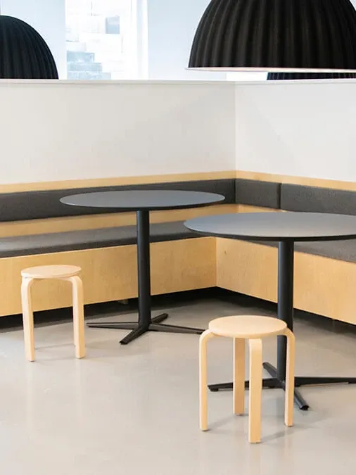 Custom-made plywood bench seating with black round tables and wooden stools, designed for modern student accommodation interiors.