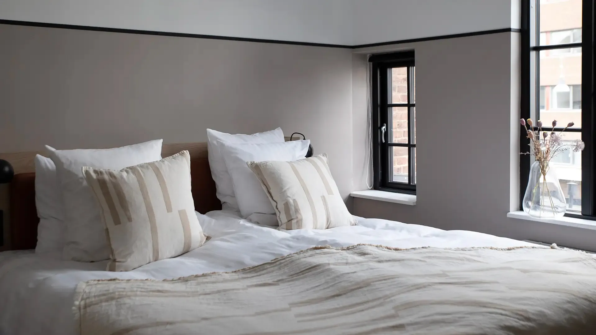 Hotel room with double bed, soft striped linen and neutral tones, showcasing a practical and elegant interior concept for modern hospitality.