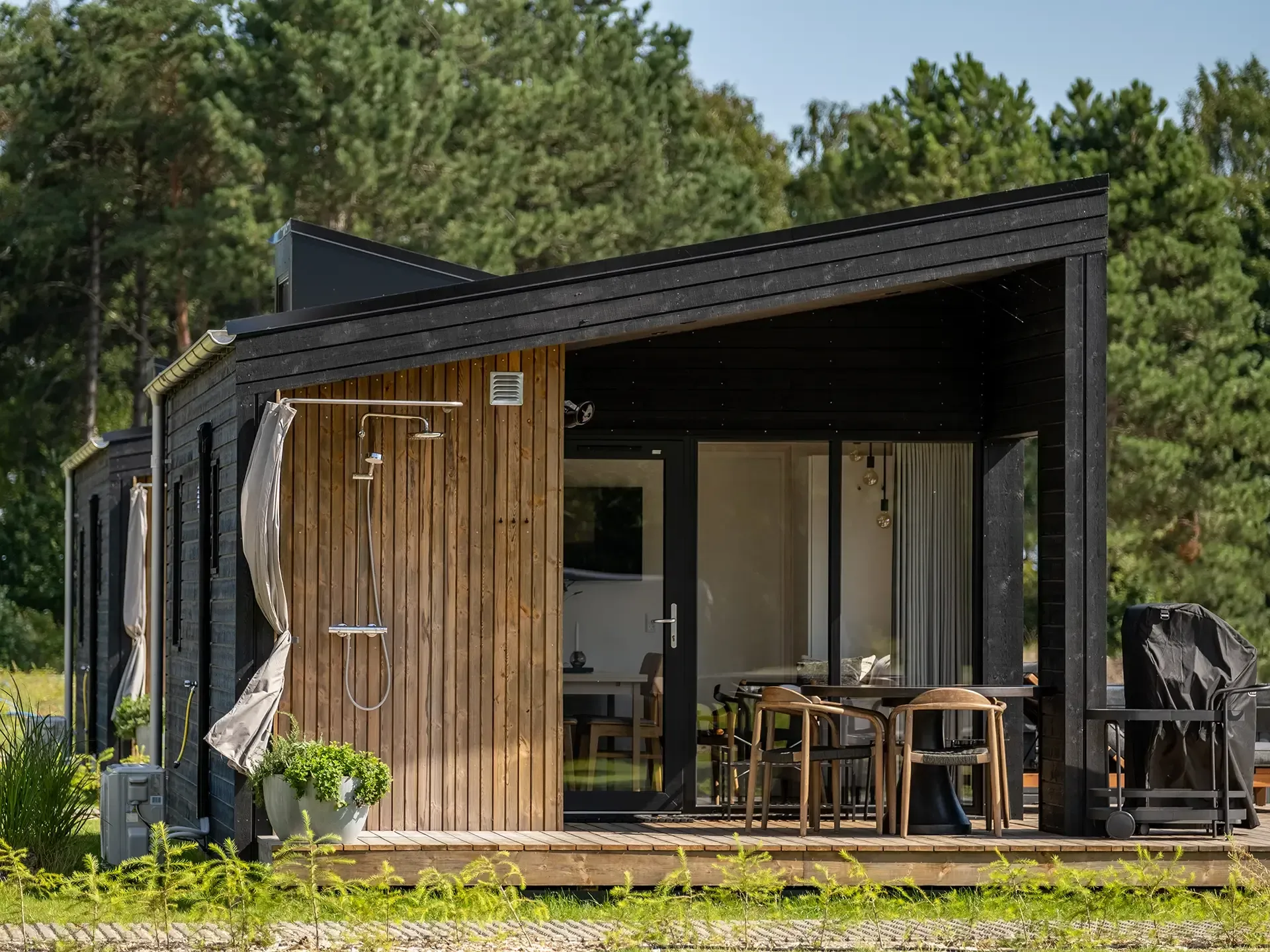 Scandinavian camping cabin with covered wooden terrace, outdoor shower and designer garden furniture.