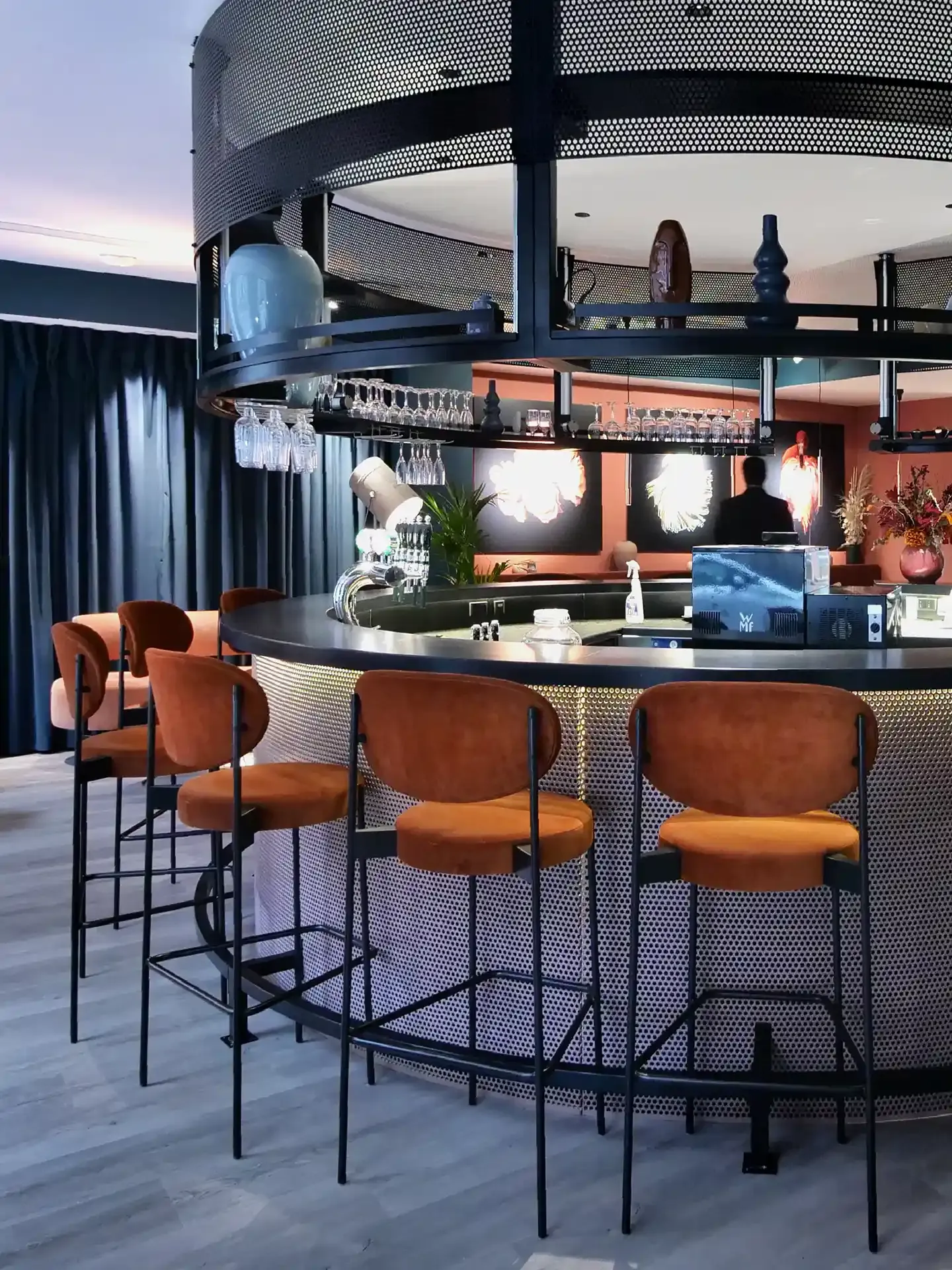 Bespoke hotel bar in perforated black metal with suspended shelving and sculptural details.