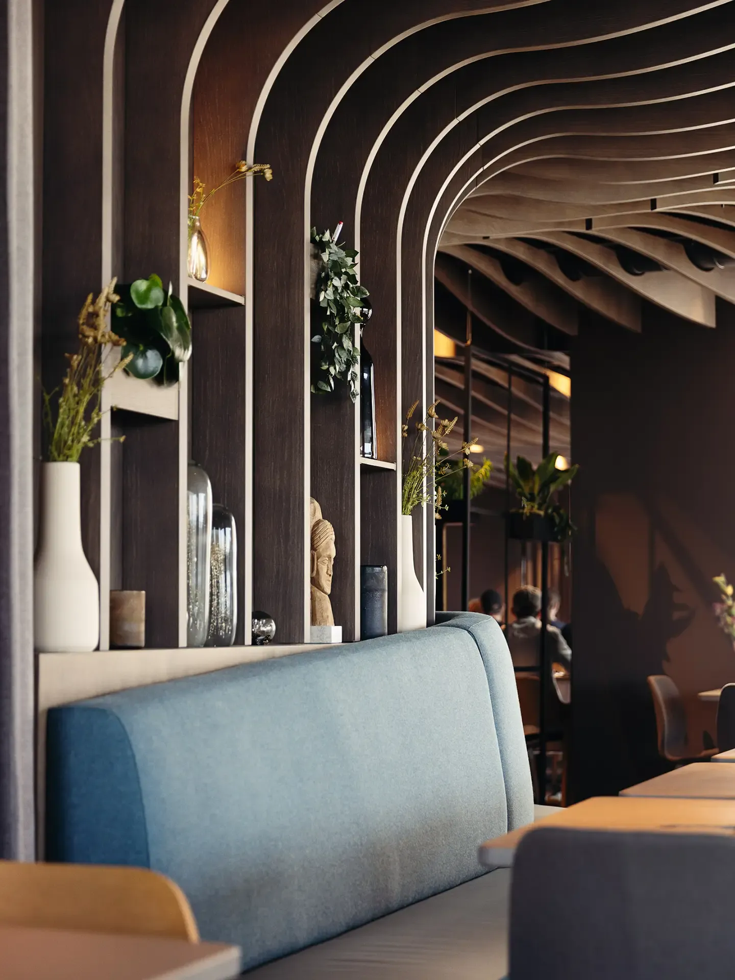 Restaurant interior with custom wall paneling and upholstered blue sofa, merging acoustic comfort with Nordic aesthetics.