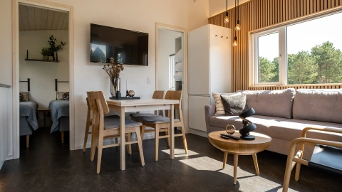 Stylish living and dining area in Nordic camping cabin, furnished with Scandinavian oak furniture, modern lighting and neutral tones – ideal for small vacation homes.