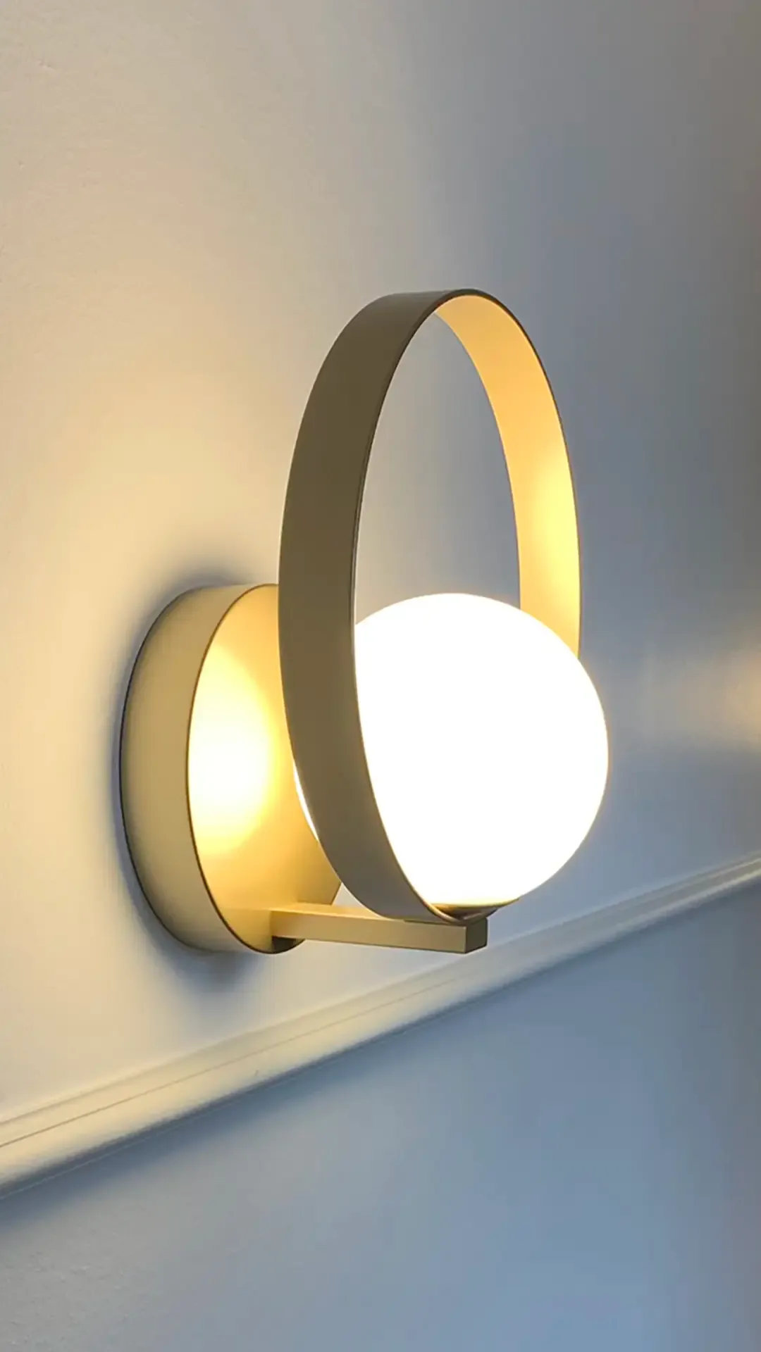 Brass wall light fixture with opal glass globe in a refined hotel corridor detail.
