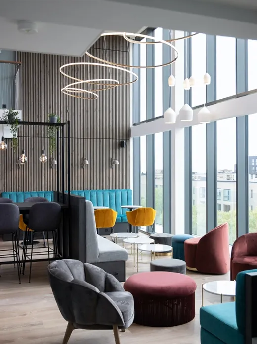 Modern hotel lounge seating area with armchairs, poufs, and decorative ceiling light rings.