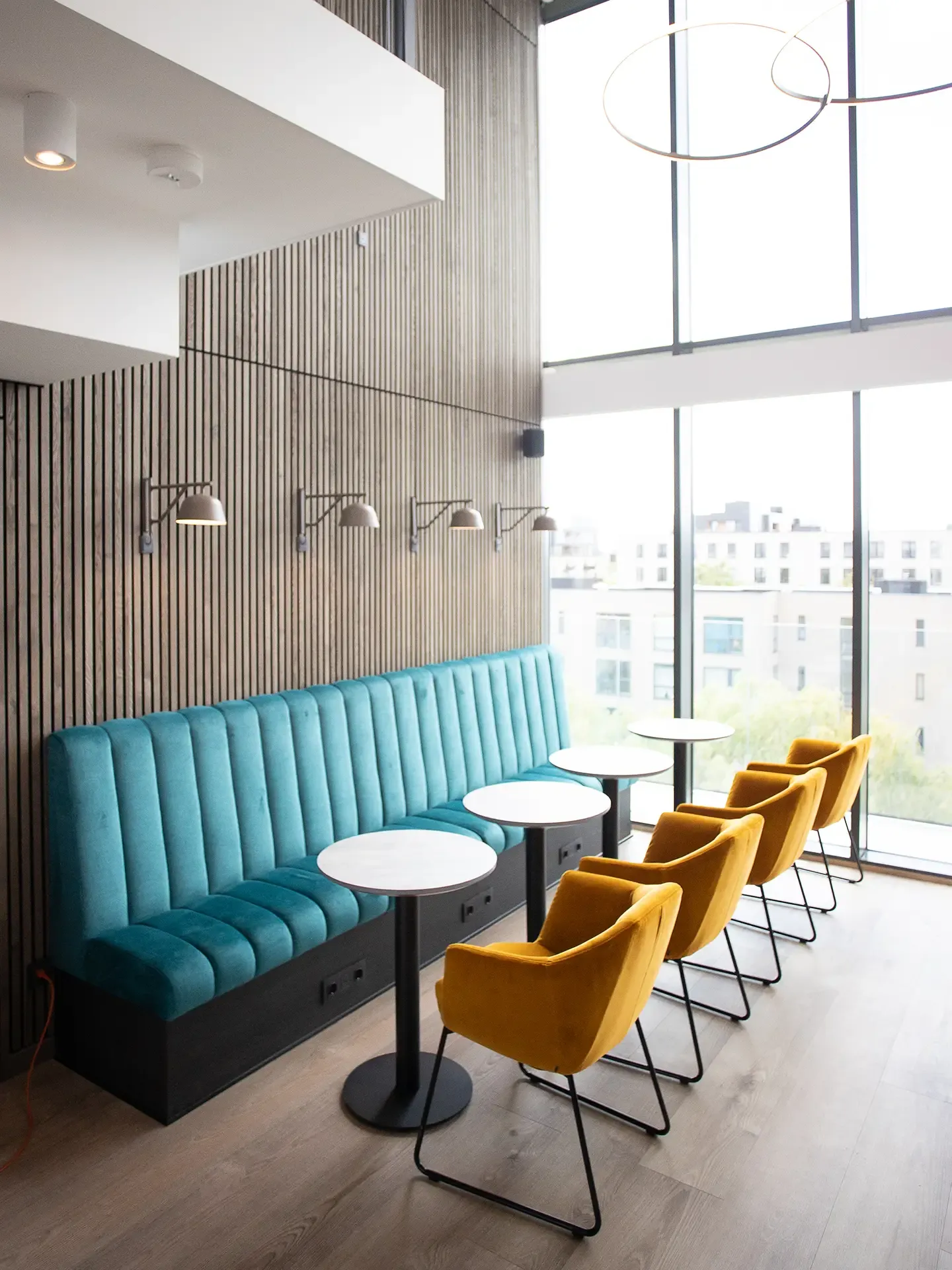 Lounge seating area with yellow chairs and round tables by hotel window.