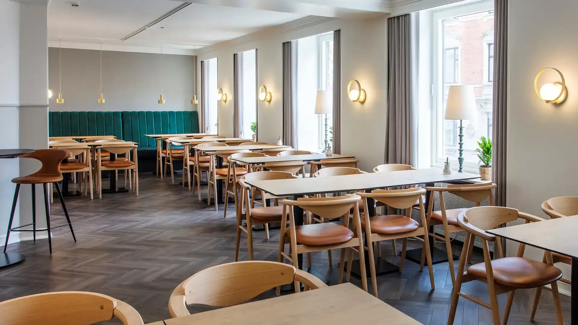 Restaurant area with oak tables, brass lamps and green upholstery, Nordic design.