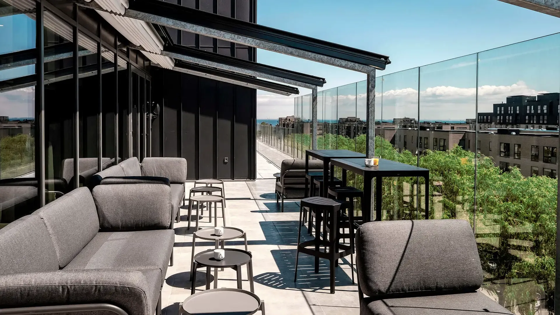 Rooftop terrace with lounge seating, tables, and sea view from a modern hotel.