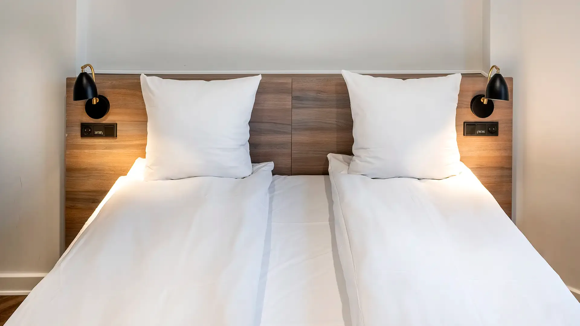 Twin bed hotel room with bespoke white linen headboard and minimalist lighting.