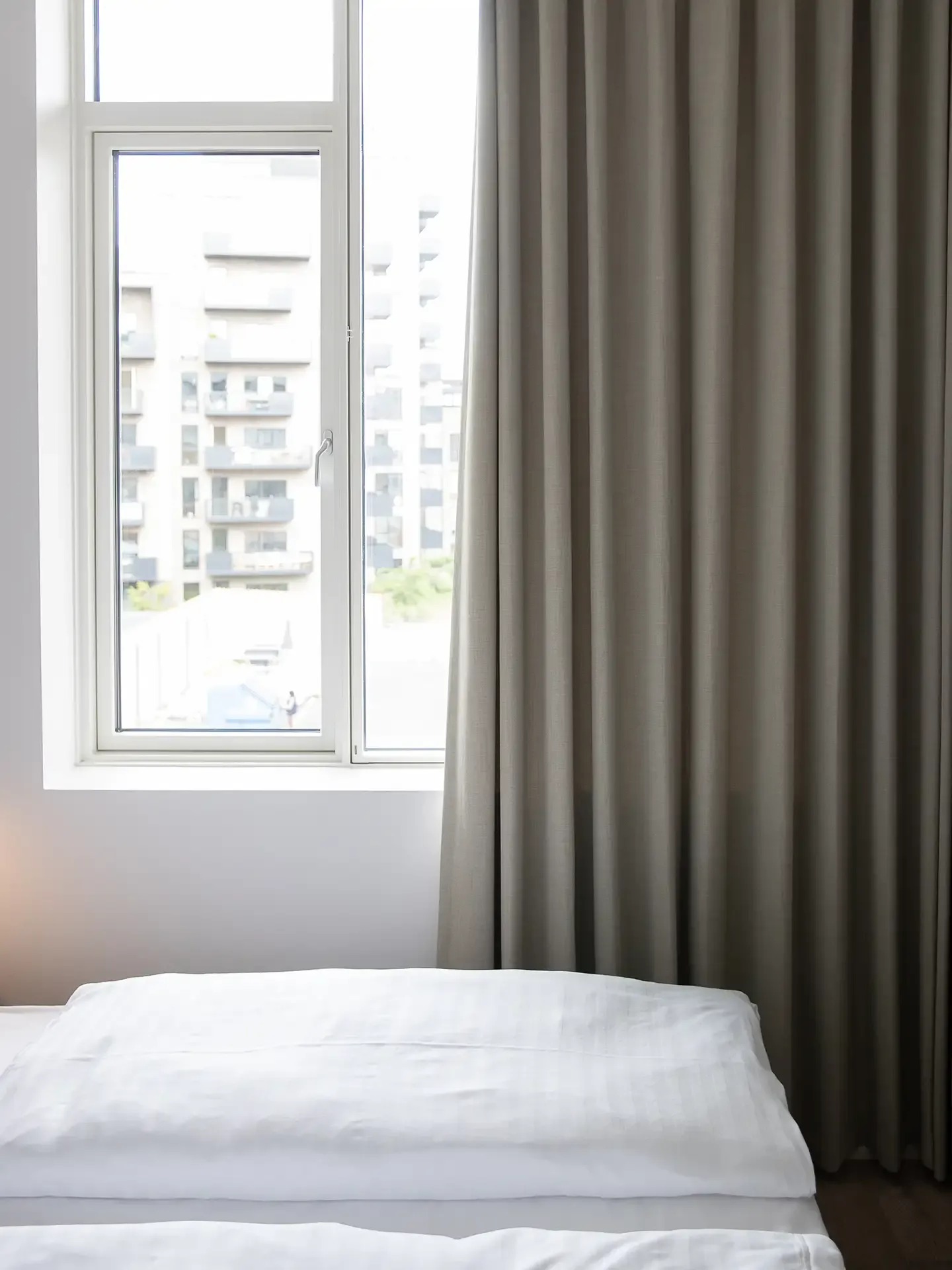 Double bed hotel room with city view from large window.