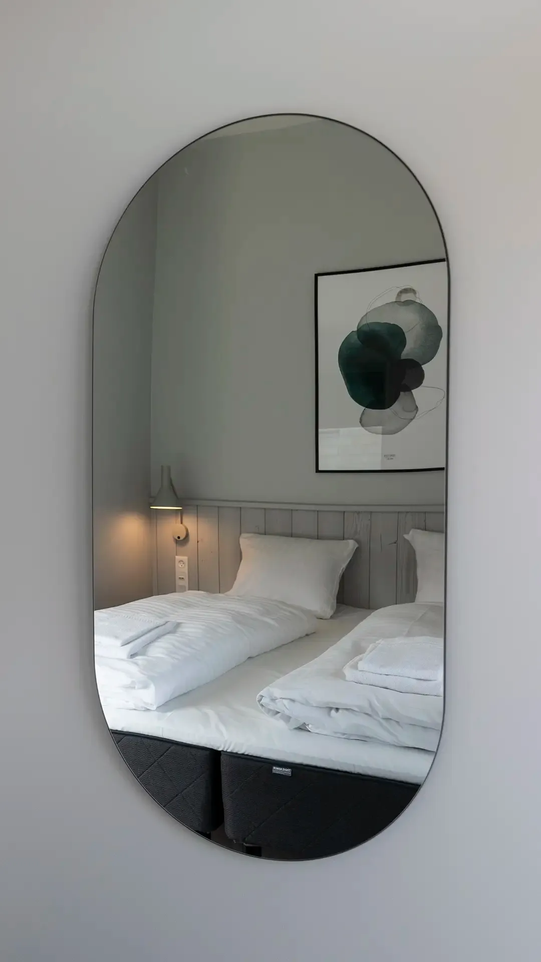 Modern hotel room interior with wall mirror and soft neutral tones.