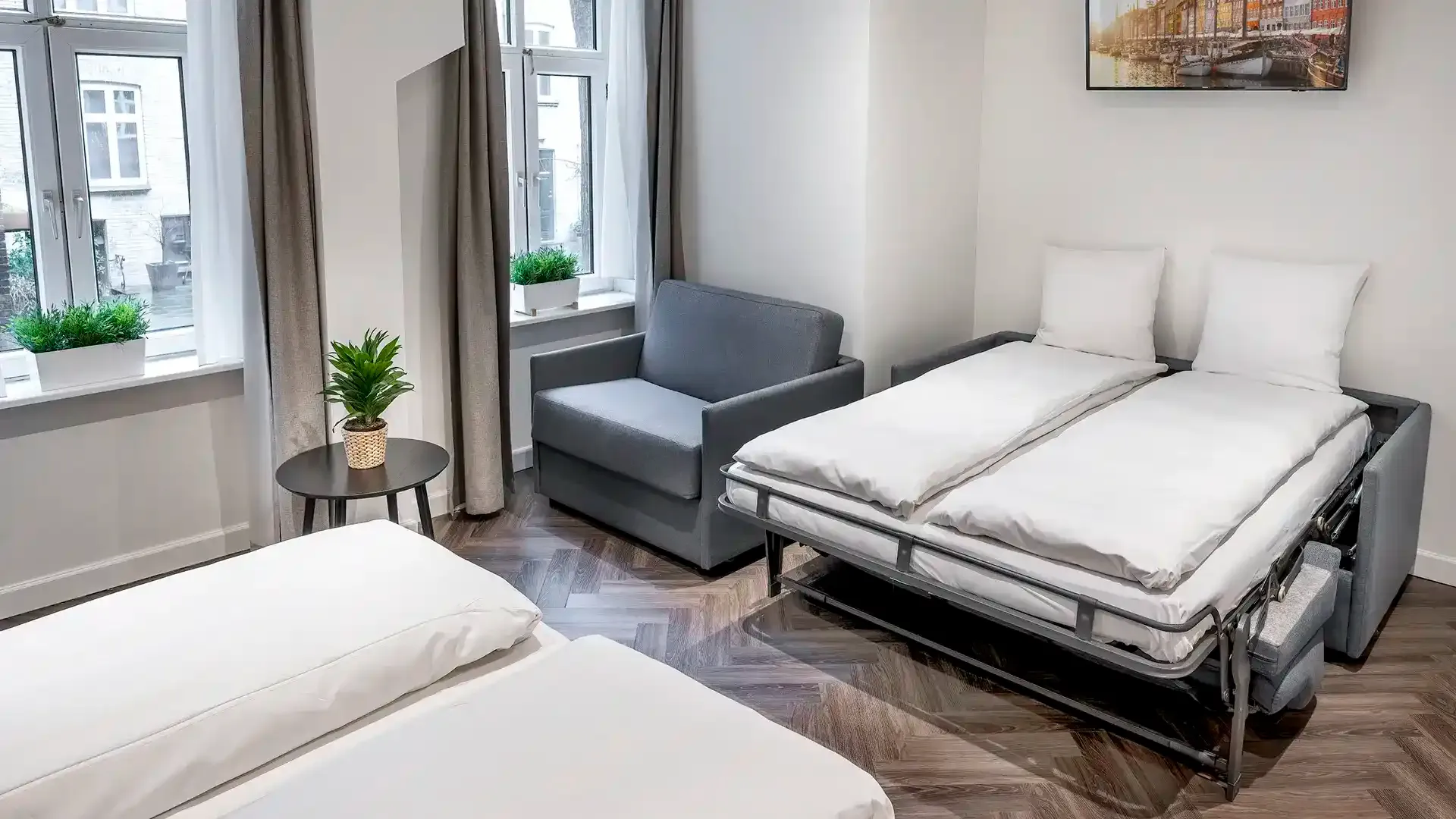 Convertible sofa bed unfolded as extra hotel bed with white linen — efficient interior design for compact urban hotel rooms.