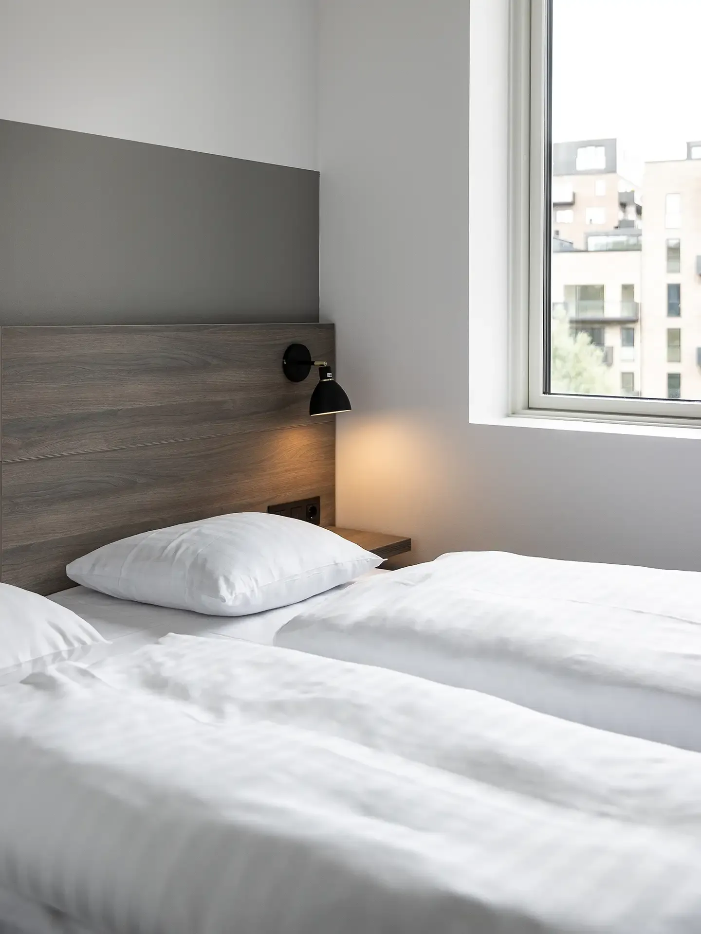 Twin bed hotel room with light wood headboard and bedside lamps.