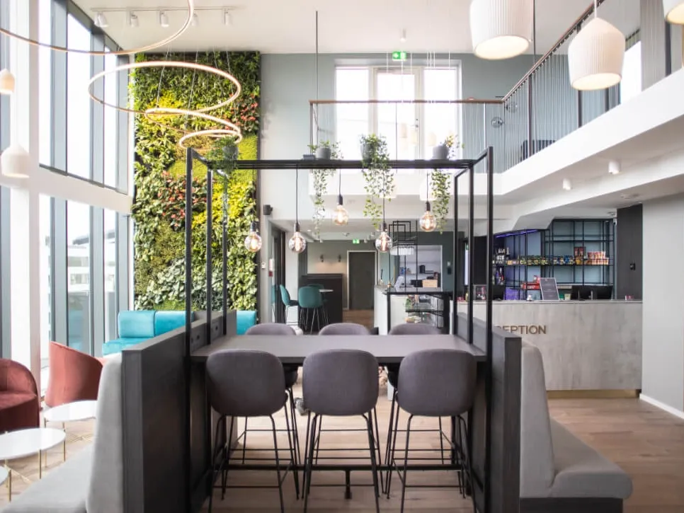 Skybar and lounge area in modern hotel with high table seating, green wall feature, and view towards reception area.