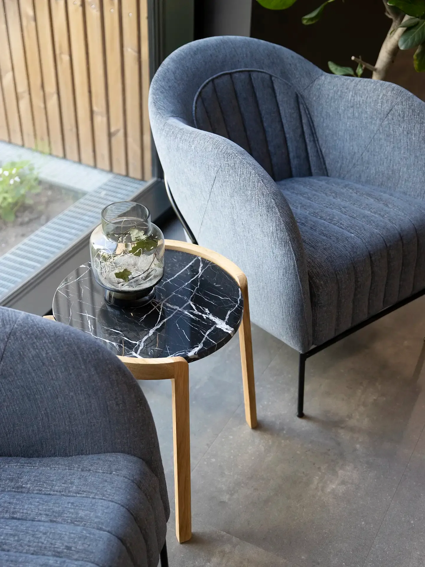 Detail view of lounge chair in soft upholstery paired with a small stone-top table, ideal for refined waiting or relaxation areas.