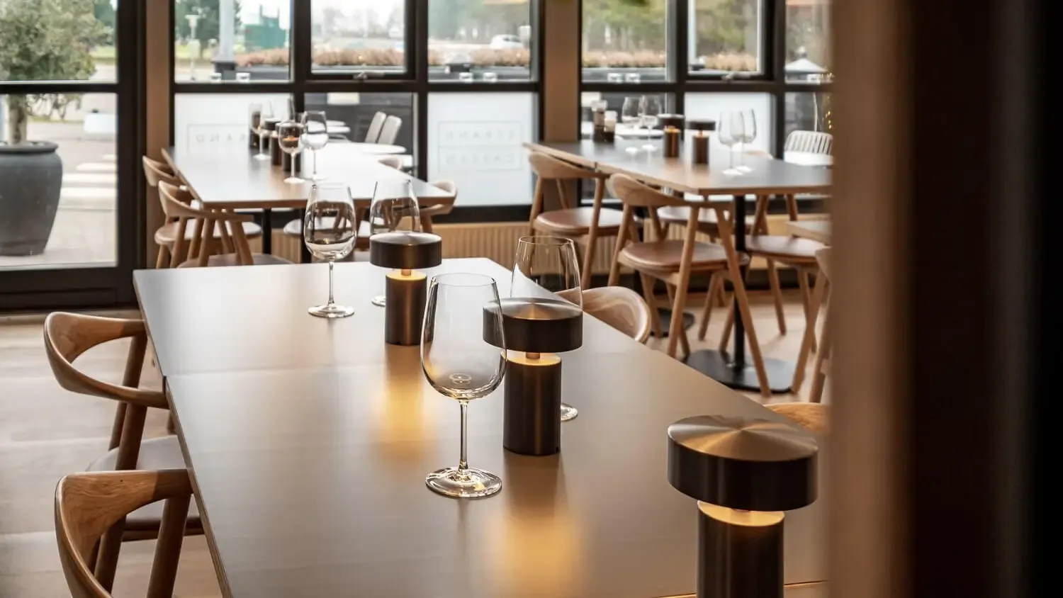 Elegant restaurant interior with LED table lamps and wine glasses, styled in warm Nordic tones – perfect for dining spaces in resorts and camping facilities.