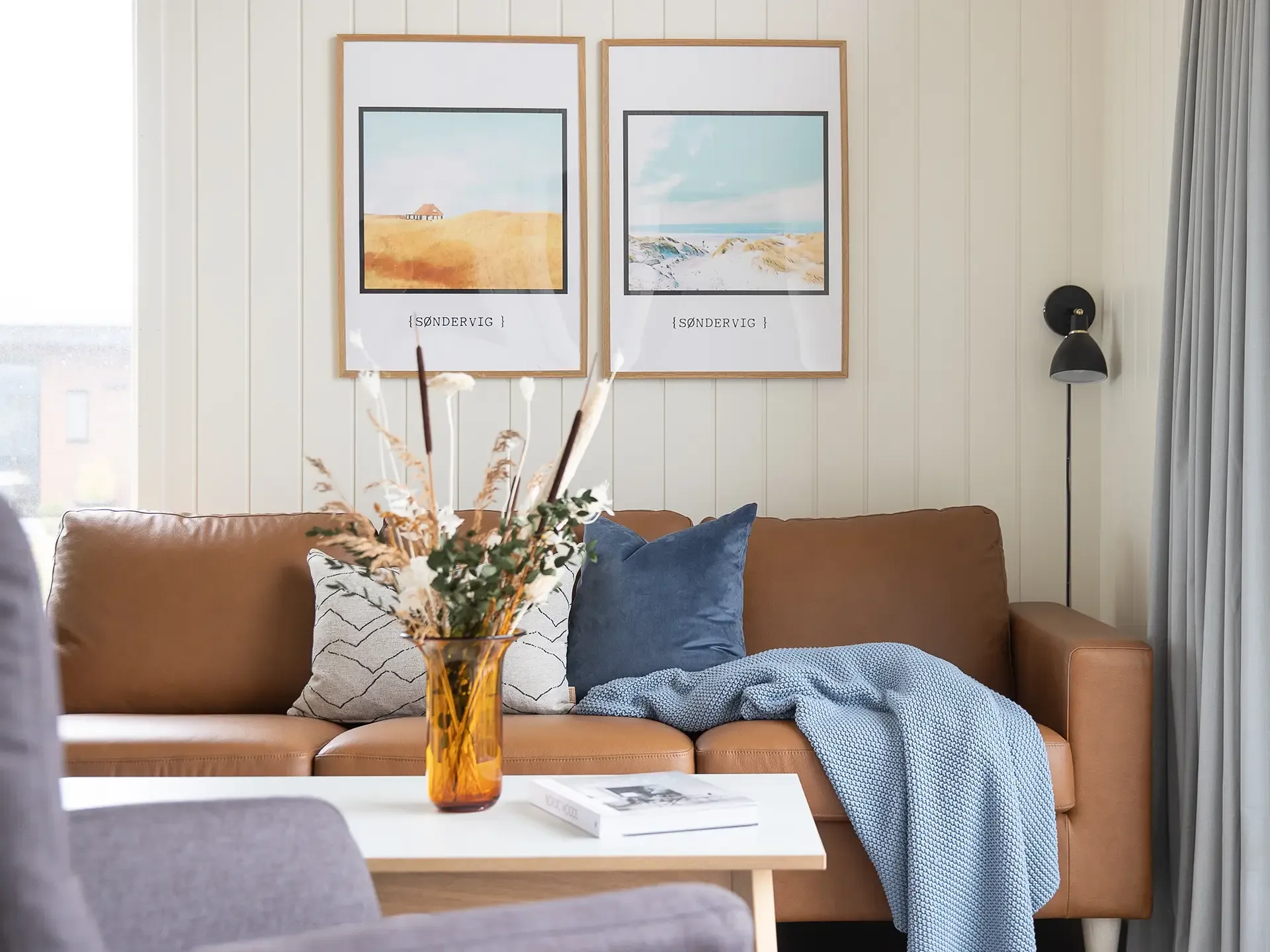 Nordic holiday home living room with cognac leather sofa and art posters, designed for modern comfort.