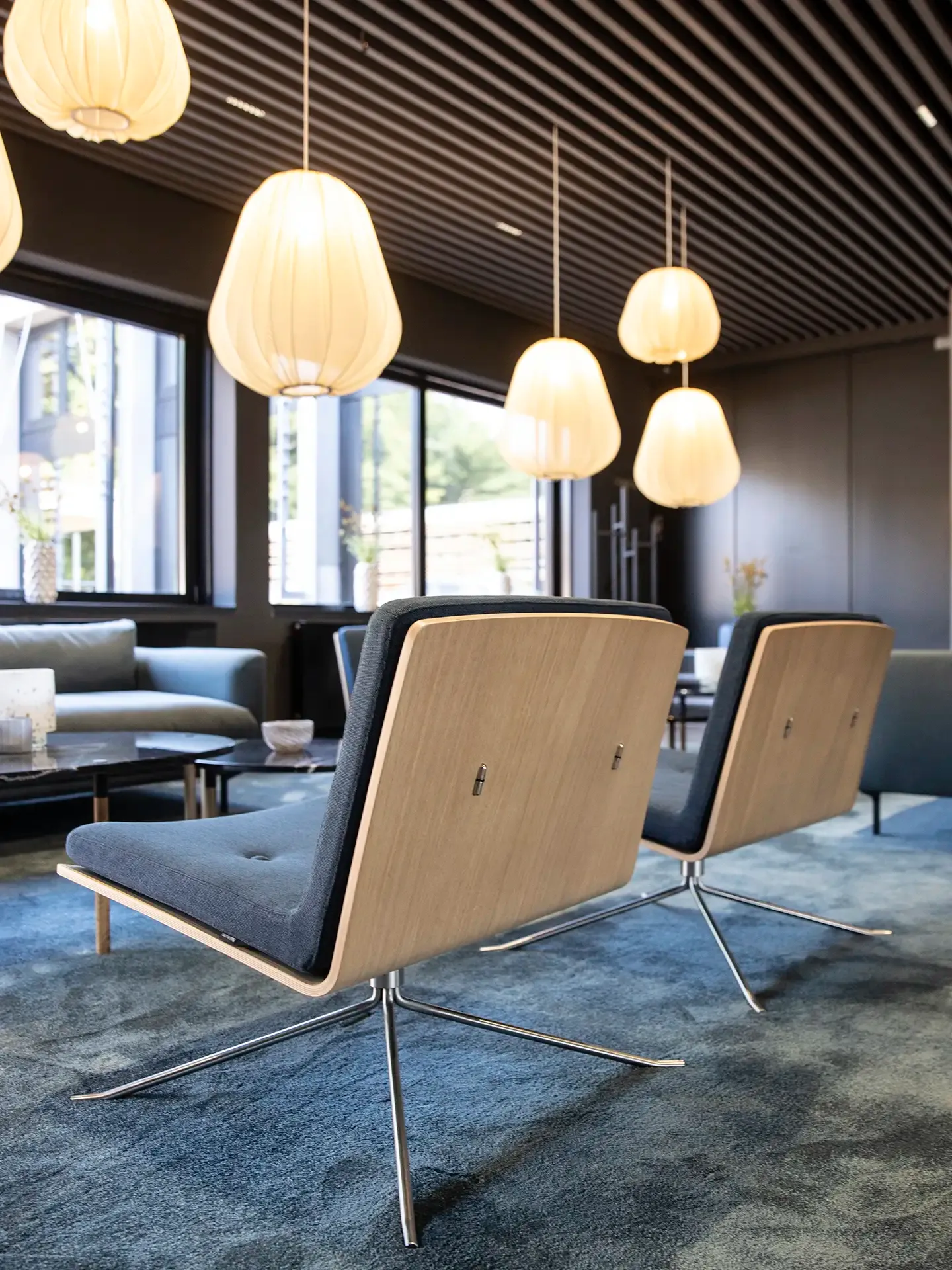 Stylish lounge setup with oak-backed chairs in blue fabric beneath Bolia pendant lighting — refined Scandinavian interior for modern showroom.