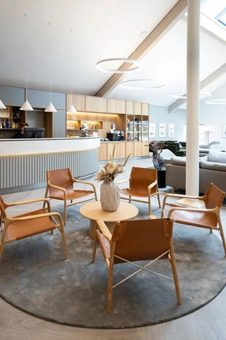Hotel lounge with leather chairs and a round wooden table. Custome-made reception counter in elegant nordic design.