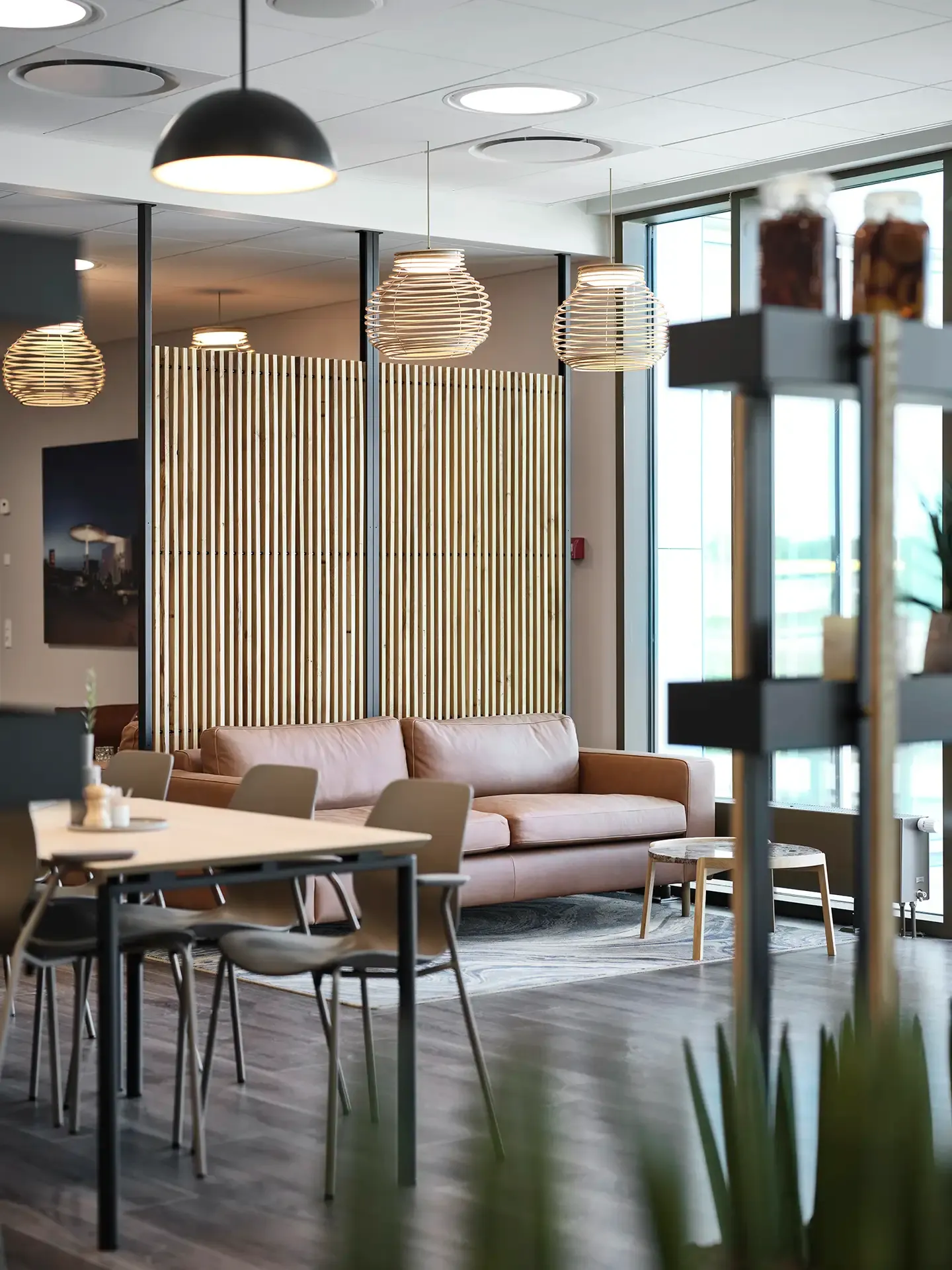 Office lounge and dining area with leather sofa, wooden accents and Nordic design, combining comfort and professional aesthetics.