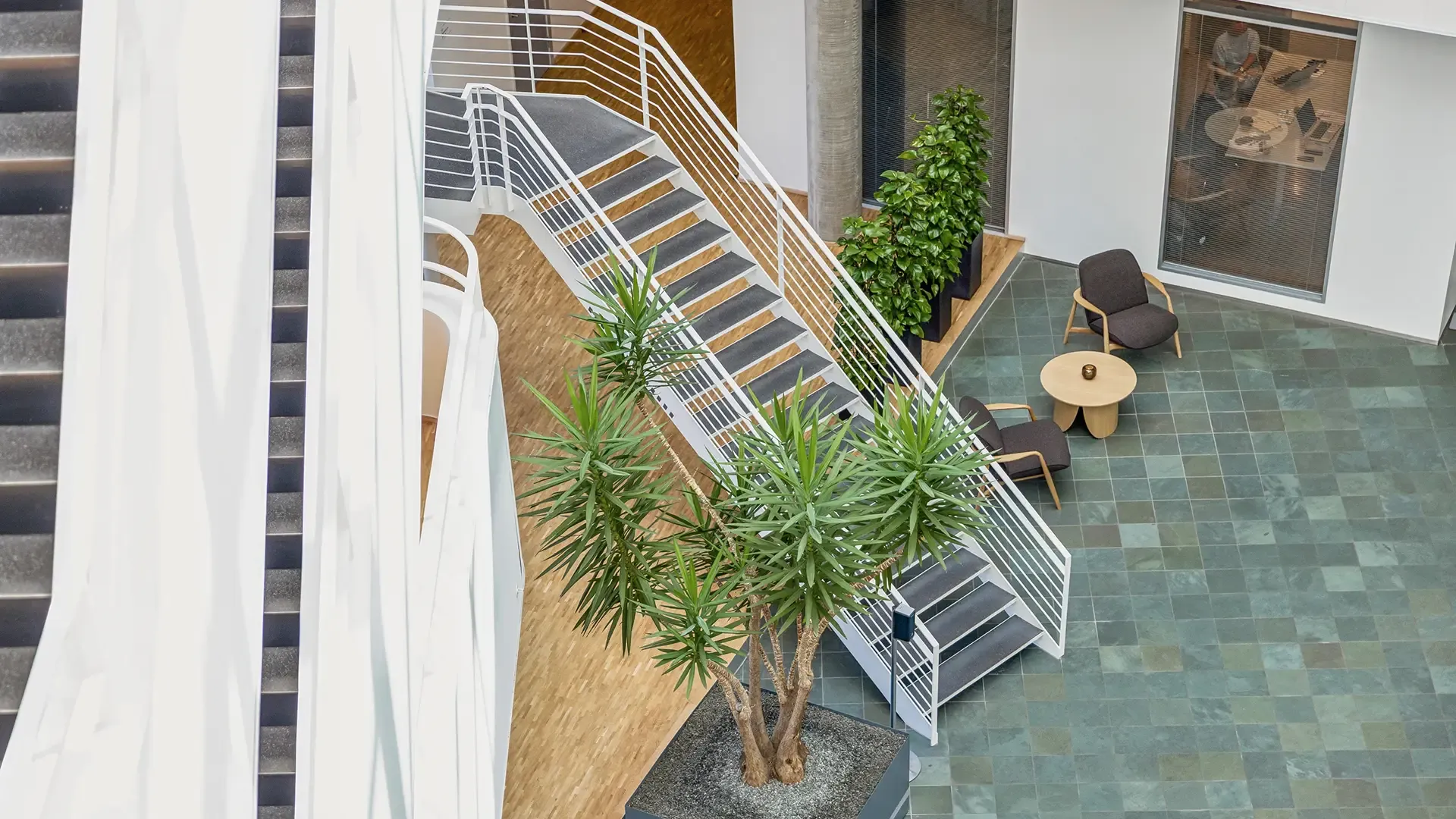 Office atrium with stairs, integrated greenery and Bolia lounge chairs, combining architectural flow with interior design.