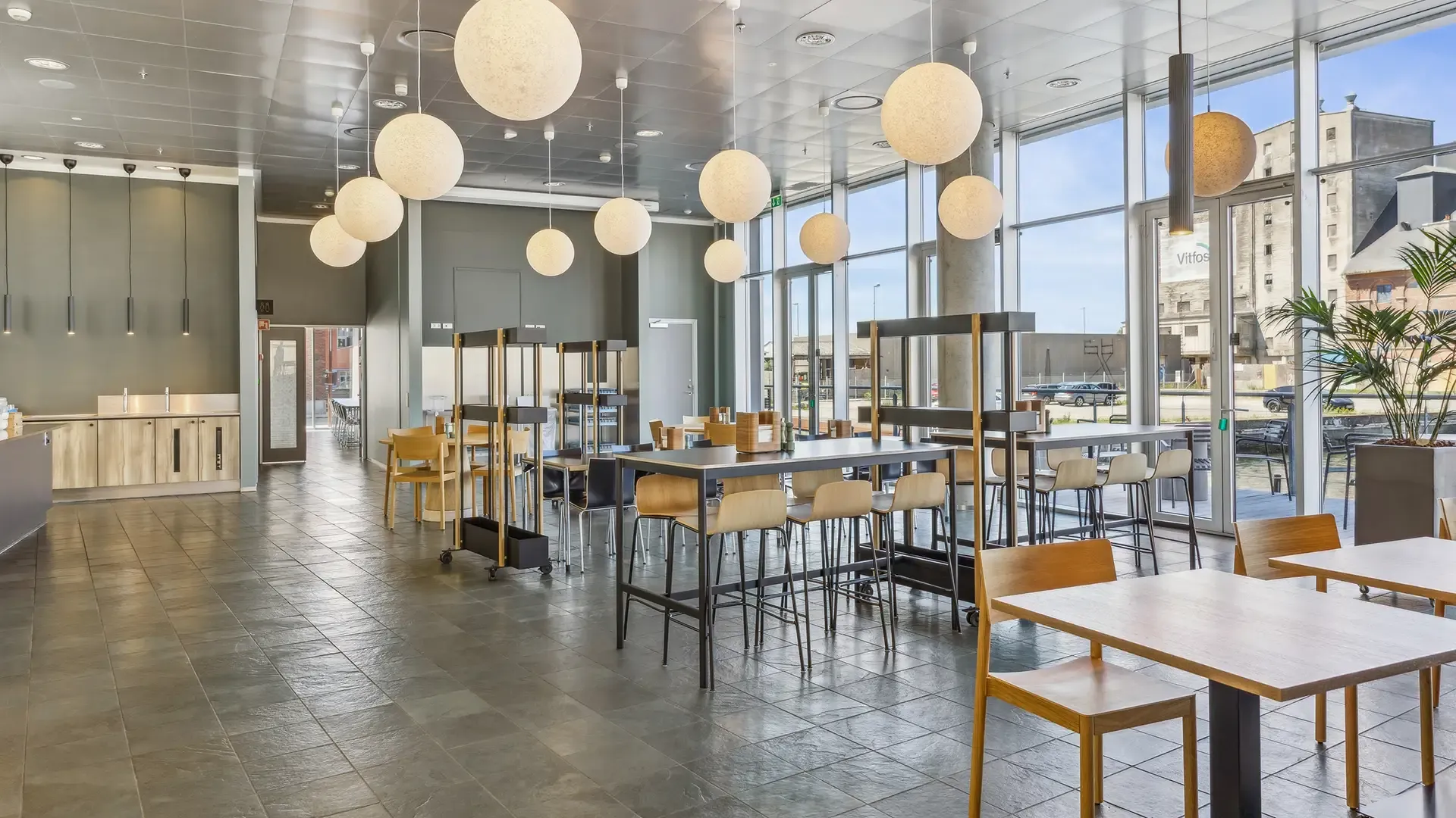 Corporate canteen with Scandinavian wood furniture and modern lighting, designed for large office dining solutions.
