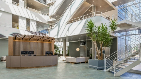 Custom-made office reception desk with wood panels in a bright atrium foyer, emphasizing corporate identity and professionalism.