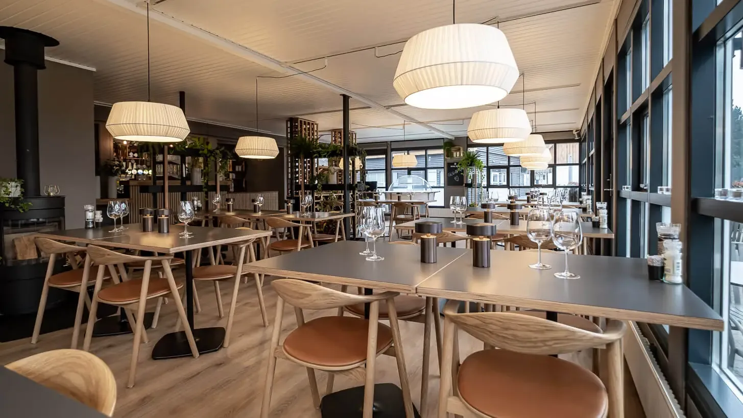 Scandinavian restaurant design featuring oak dining chairs with cognac leather seats, minimal table settings and cozy ambiance.