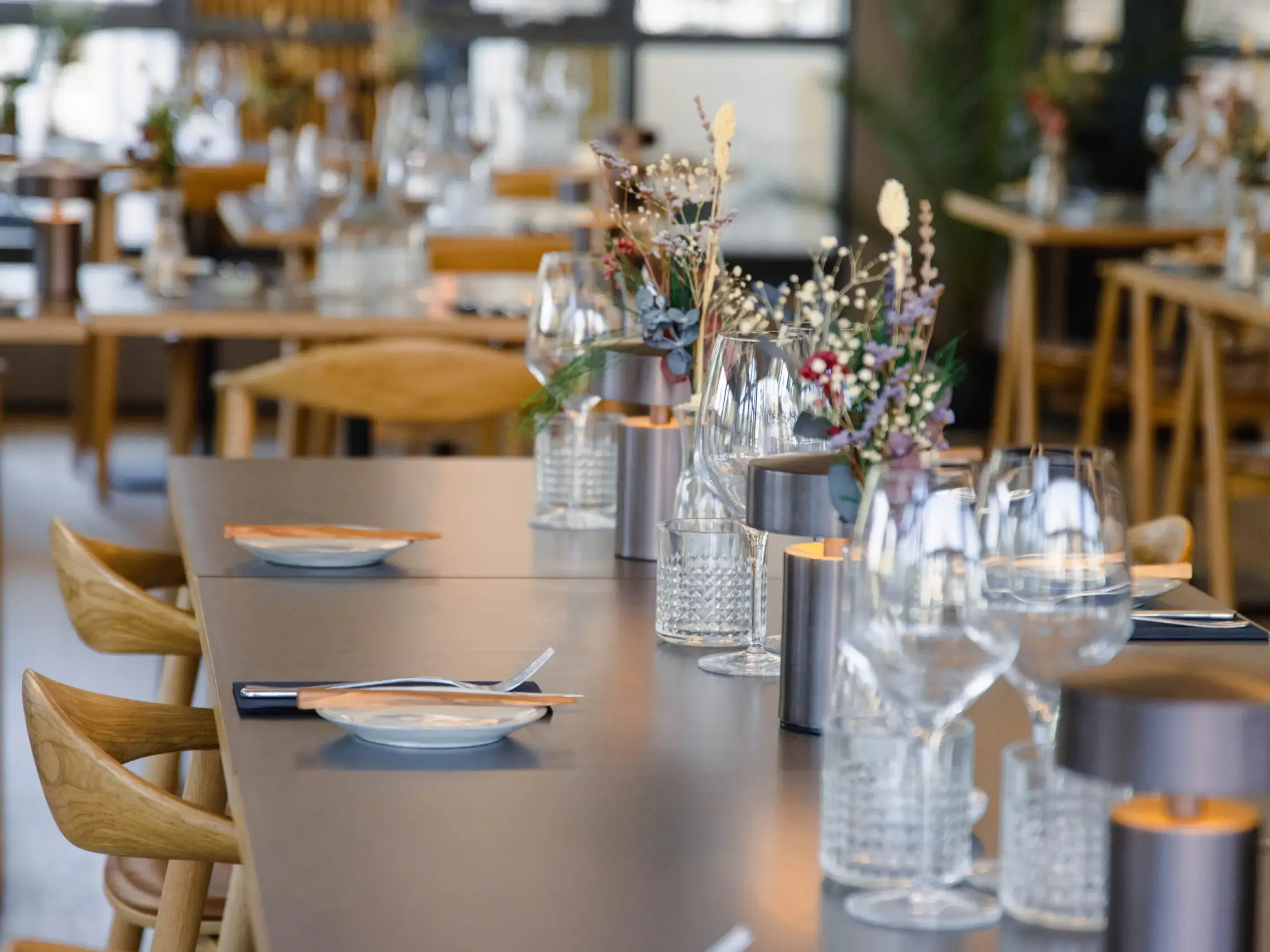 Restaurant interior design with elegant table setting featuring Nordic design with oak chairs, soft lighting.
