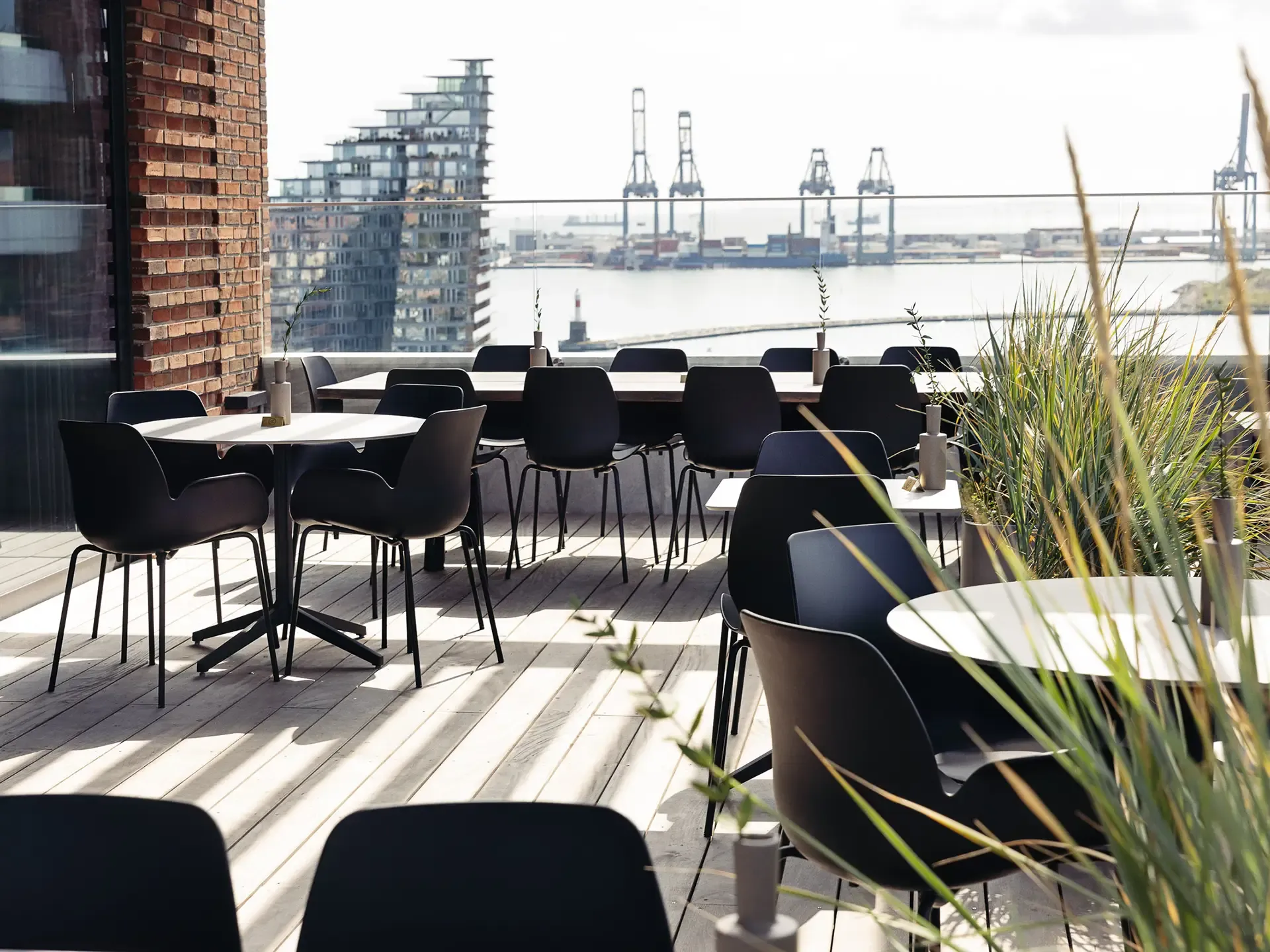 Rooftop dining space with outdoor furniture under pergola, offering panoramic port views and durable design.