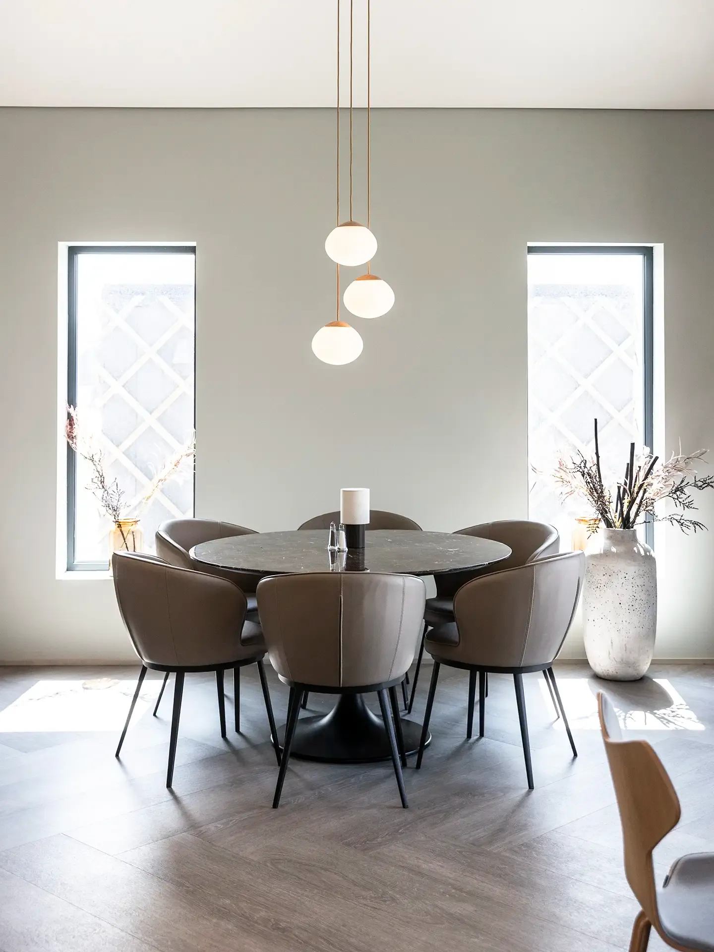 Round dining table in bright hotel breakfast setting. Leather armchairs and pendant lights.