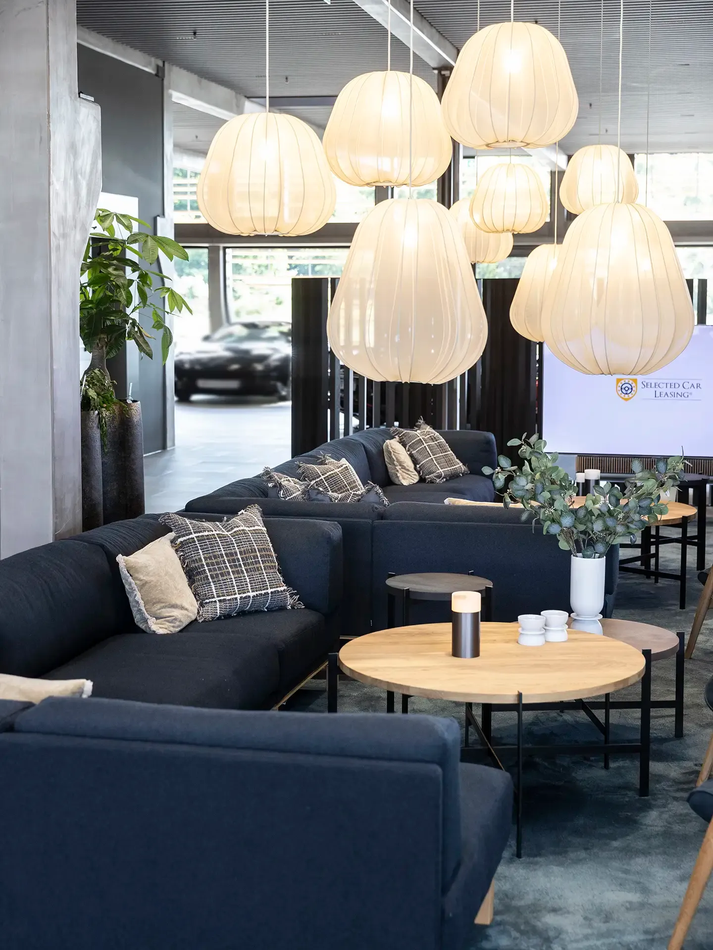 Showroom lounge with dark blue Bolia sofas, rugs, and pendant lighting in Nordic style.