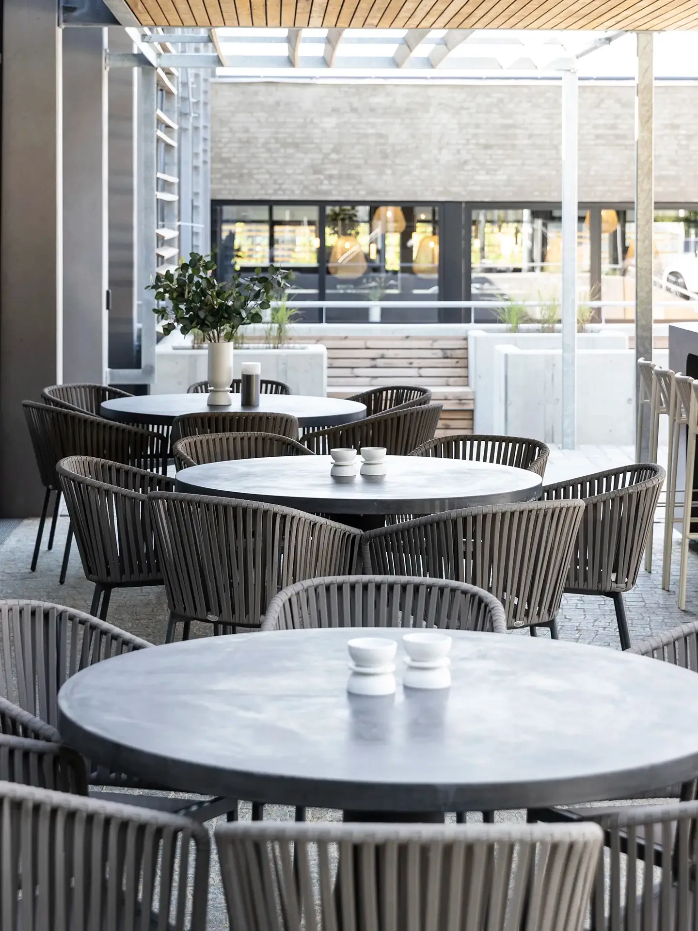 Outdoor terrace dining area with round concrete tables and Nordic chairs for showroom hospitality.