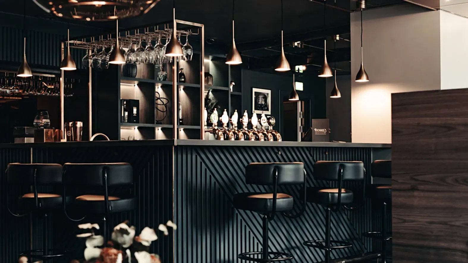 Bespoke hospitality bar design with brass pendant lighting and elegant glassware display at Hotel Royal.