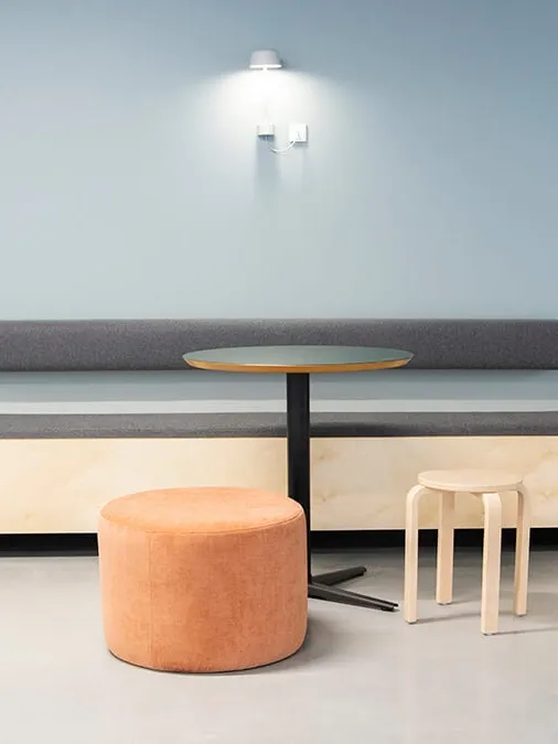 Communal seating area with built-in bench, round table, and stools, designed for flexible use in modern student living.
