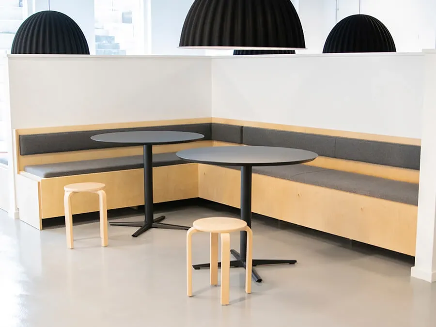 Bespoke wooden booth seating with round tables and pendant lights, crafted for Nordic-inspired student living spaces.