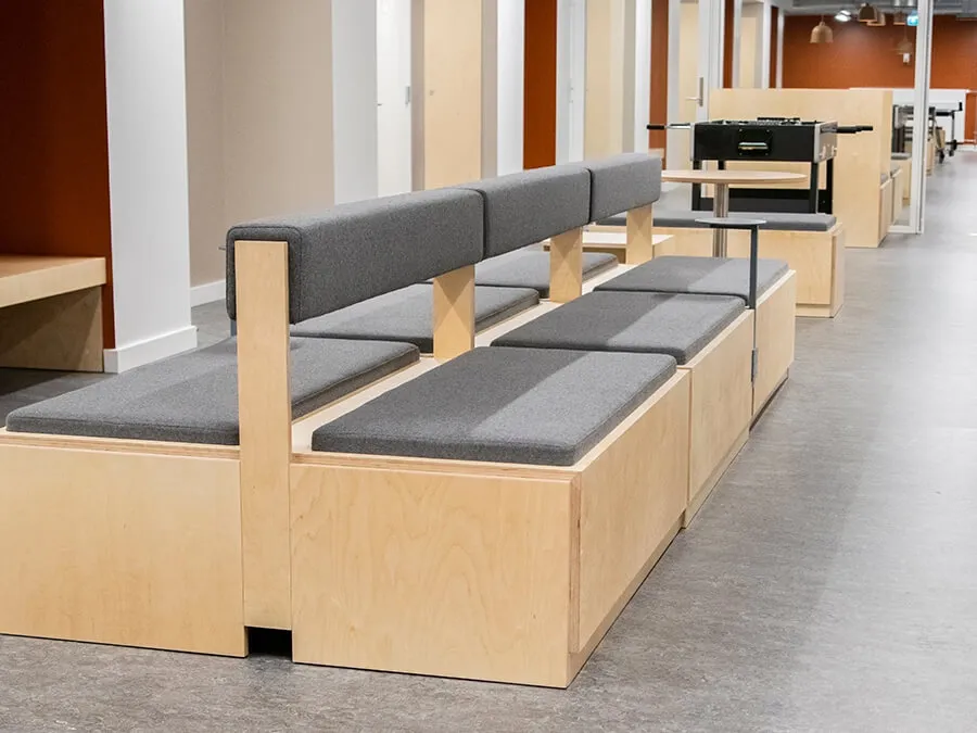 Double-sided wooden bench seating with upholstered cushions for multifunctional corridors in student housing.
