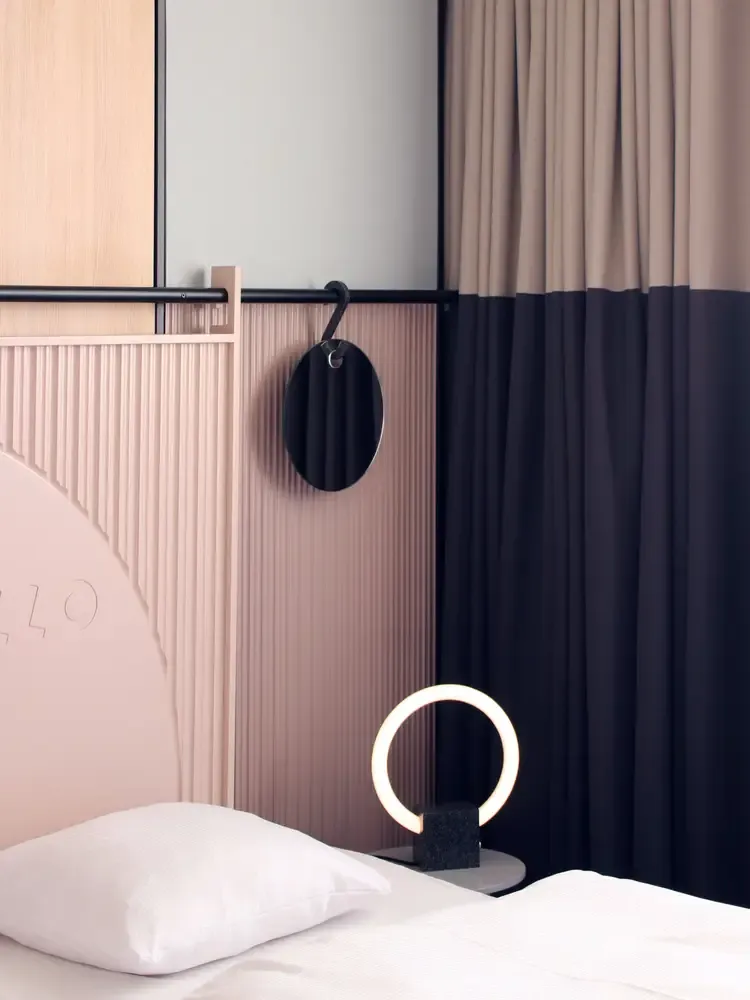 Round wall lamp in black and brass set against rose-colored panels in a hotel interior.
