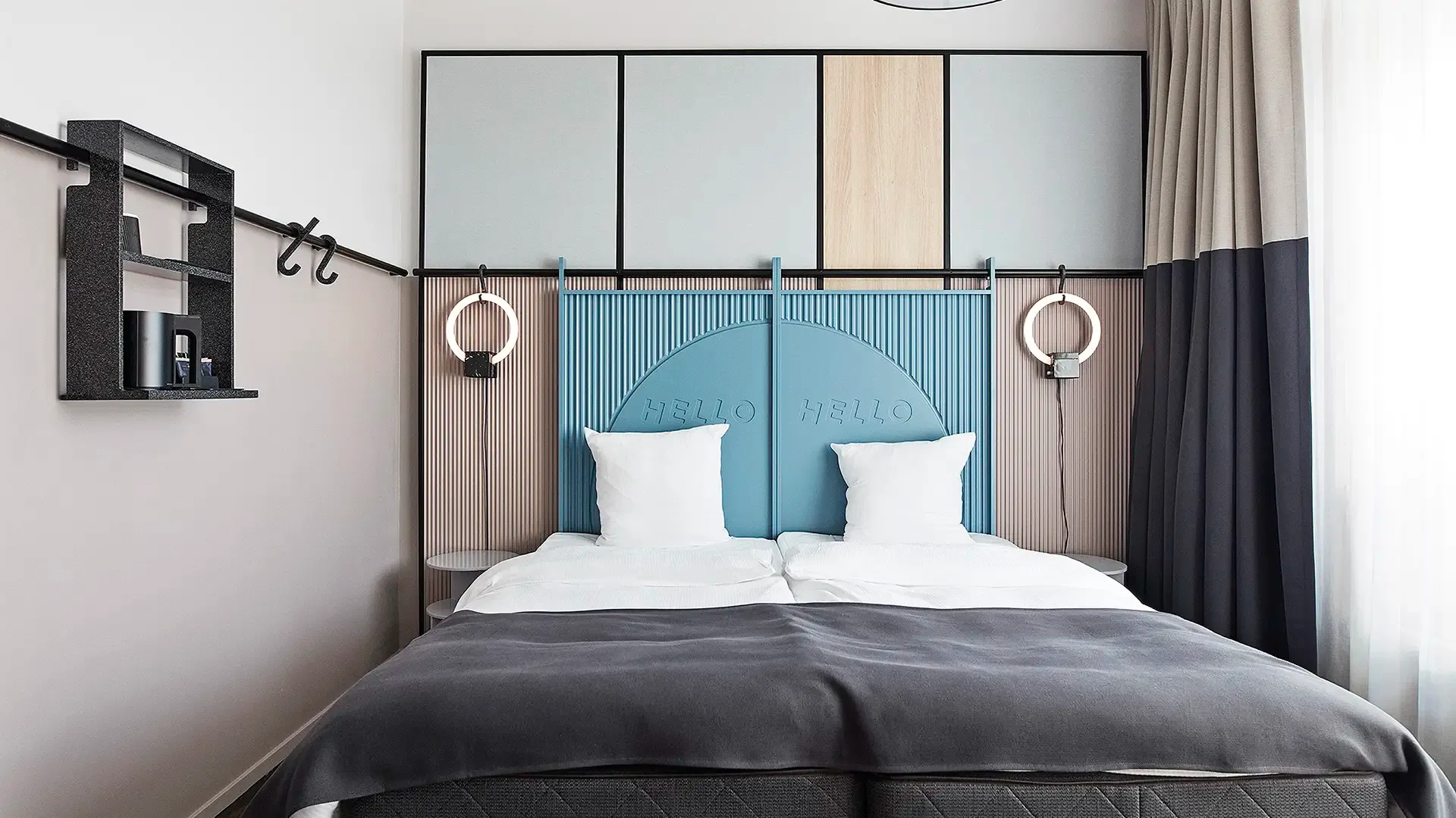 Inviting hotel room with pastel-colored custom headboard, round lamp, and light textiles.
