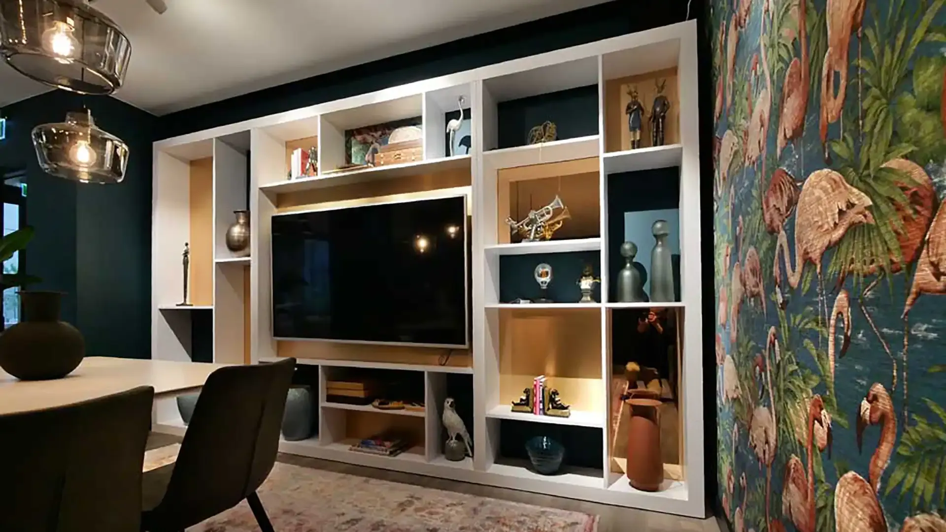 Custom-built shelving wall with integrated TV and curated objects – paired with playful flamingo wallpaper for visual identity.