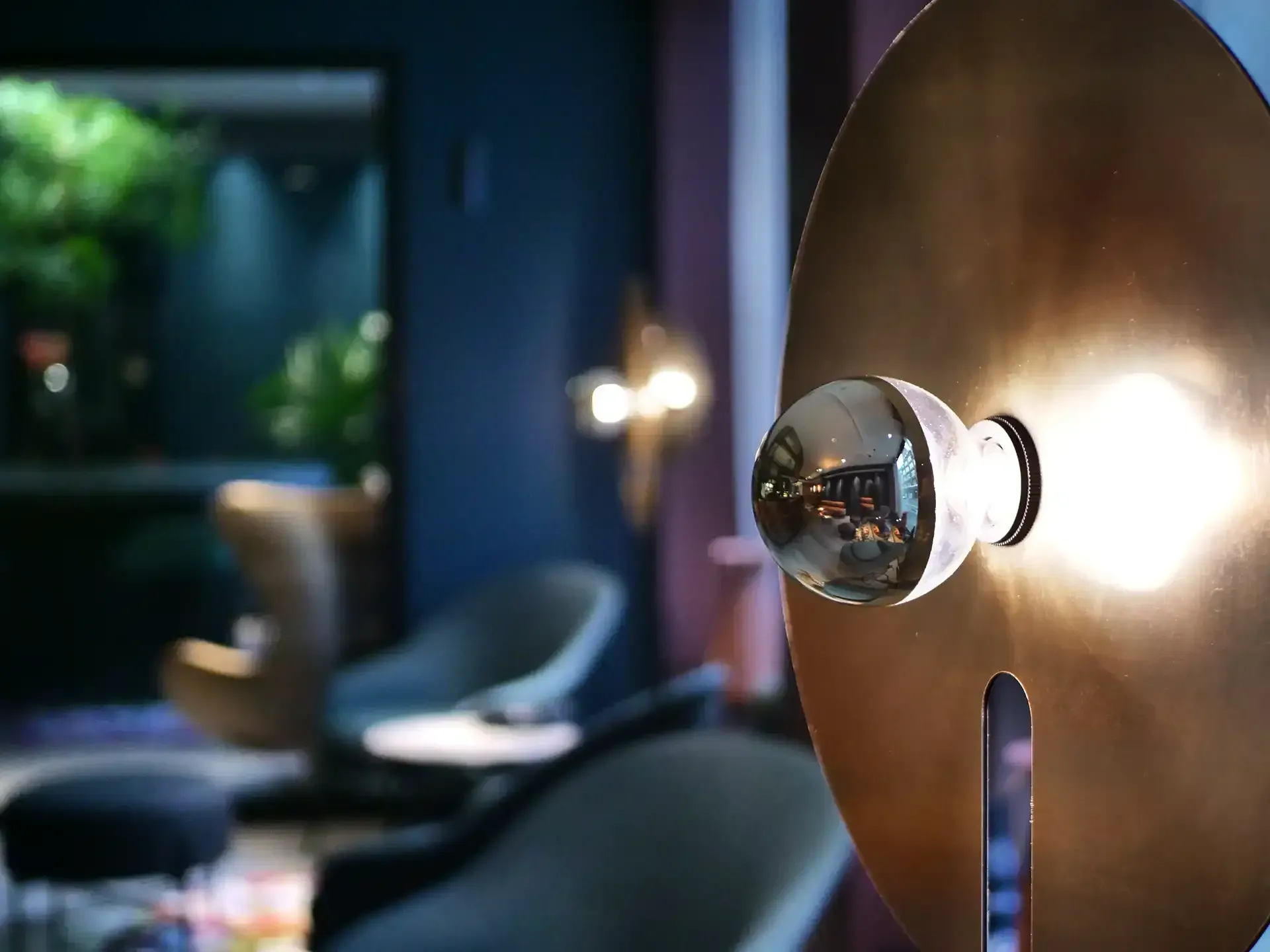 Design detail of a golden wall lamp with mirrored bulb – adding a soft glow to the dark lounge environment.