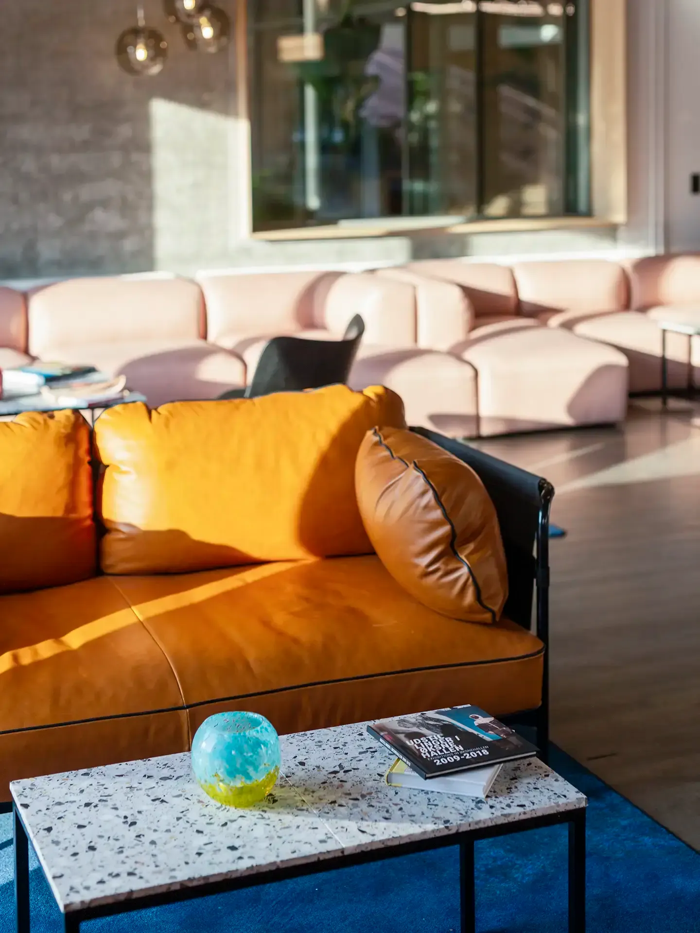 Hotel lobby lounge with bold orange leather sofa and modern design seating, creating a vibrant and inviting atmosphere for guests.