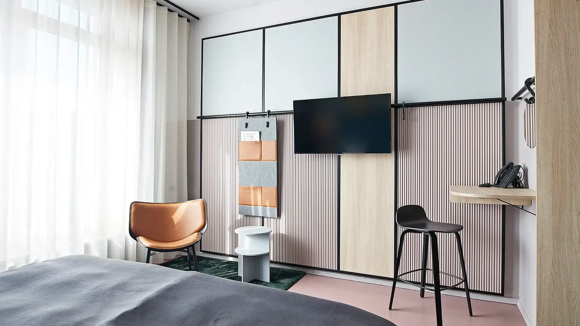Hotel room with integrated wall unit combining TV, shelving, and textile panels, designed for flexibility and comfort.