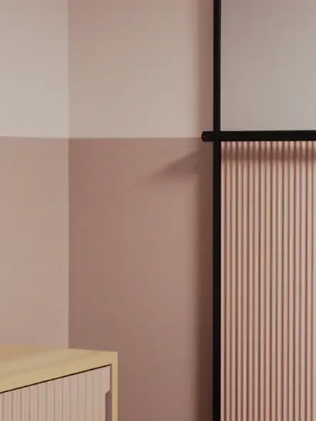 Detail view of a hotel wall concept with rose-toned paint, vertical paneling, and black metal framing.