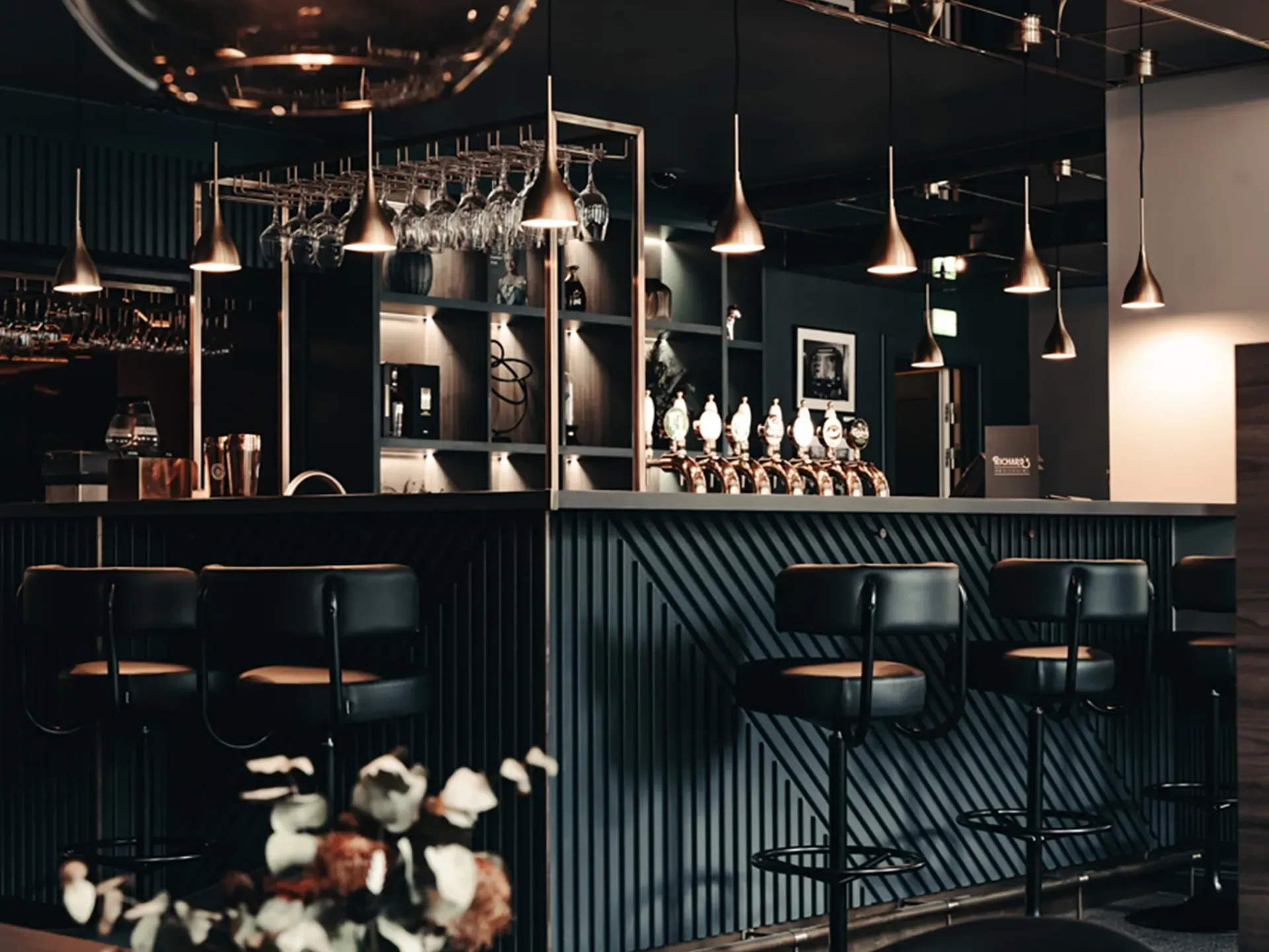 Luxury bar counter design featuring dark wood paneling and brass pendant lights at Richards Bar, Hotel Royal.
