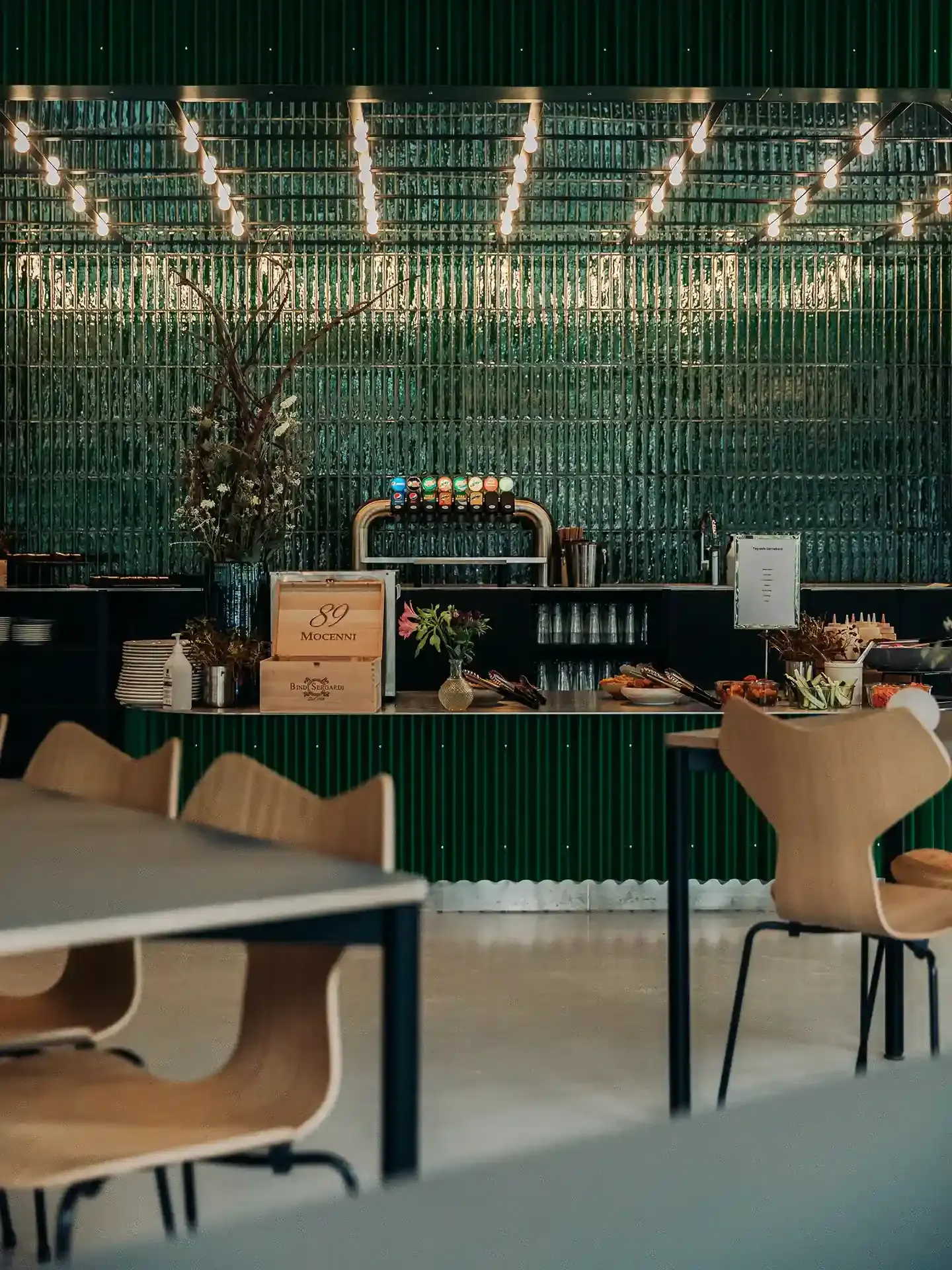 Contemporary bar interior with green tiled wall and Fritz Hansen oak dining chairs, delivering a cohesive design look and premium durability.